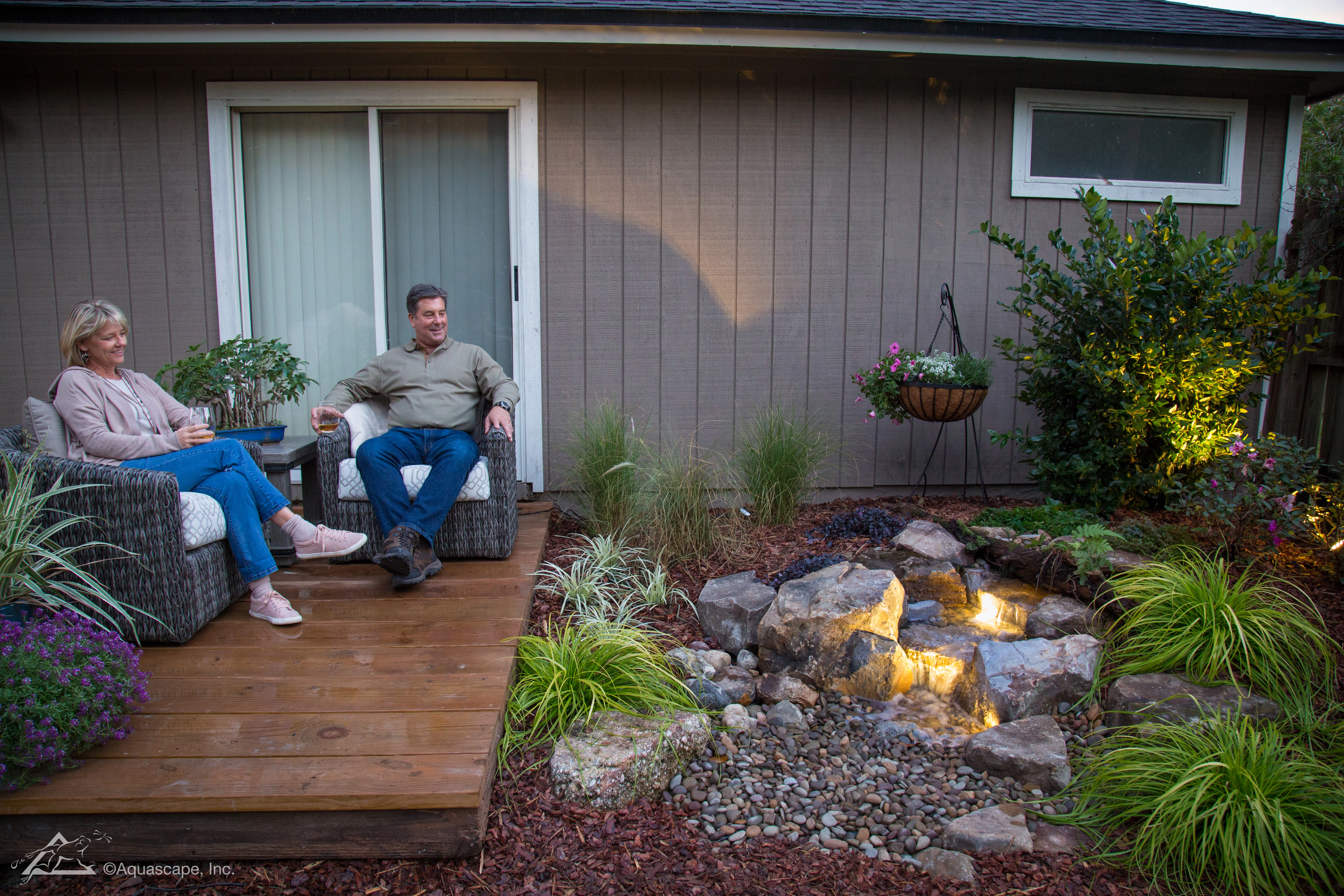Evening backyard pondless waterfall with natural stone and warm outdoor atmosphere
