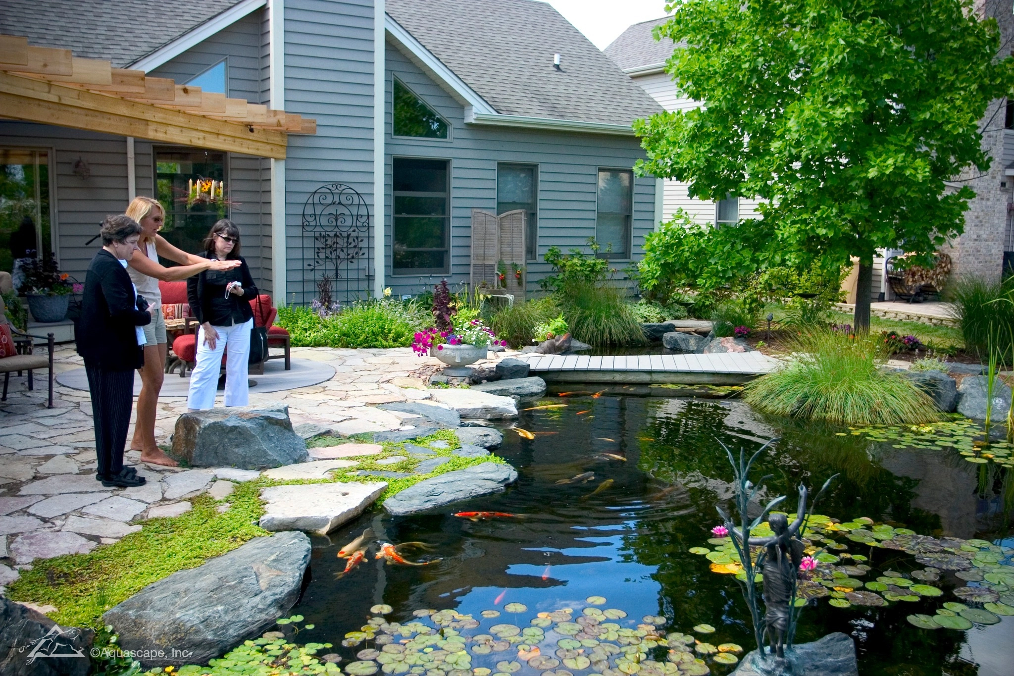 People relaxing near a backyard pond with natural water feature landscaping