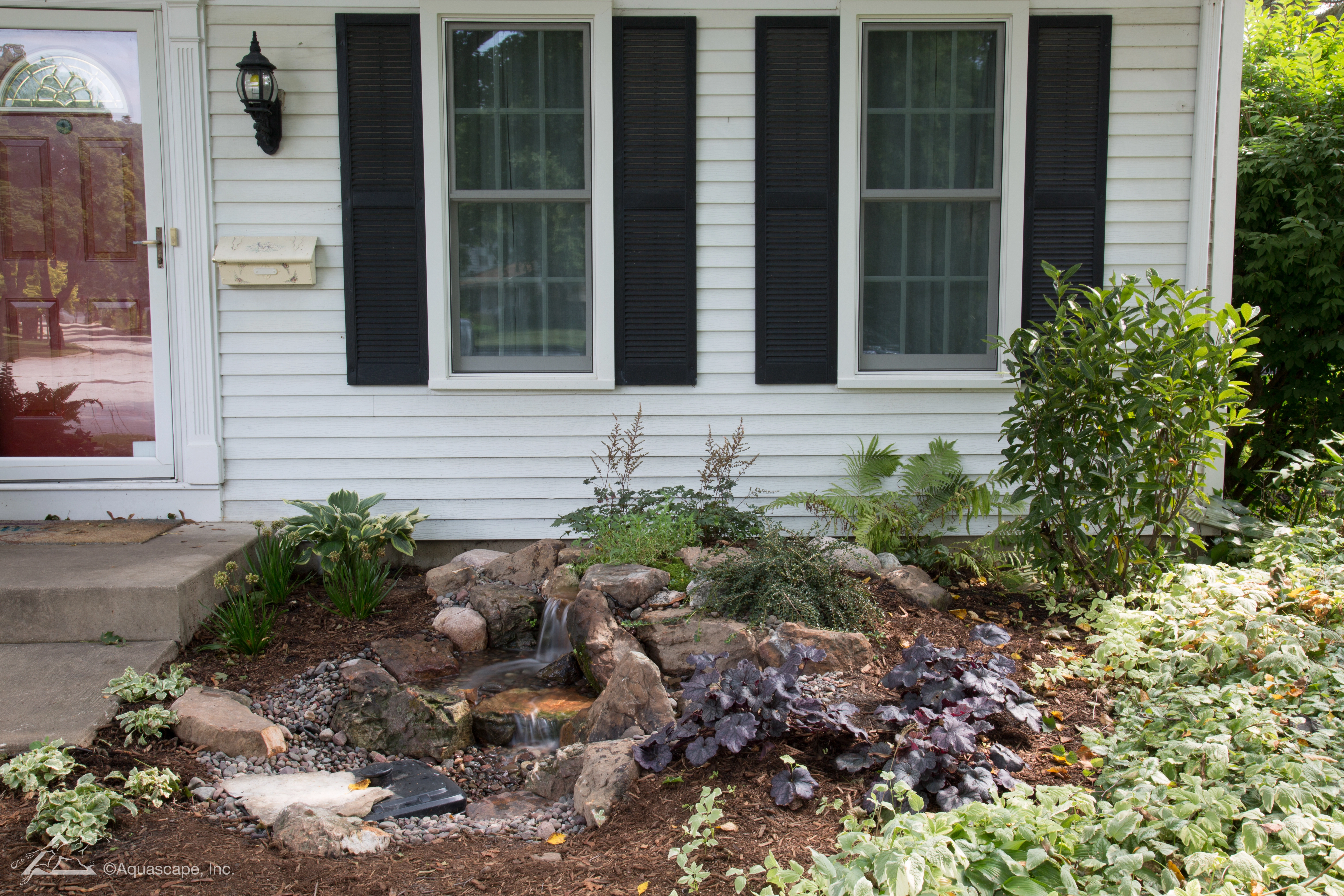 Compact pondless waterfall installed beside a residential home