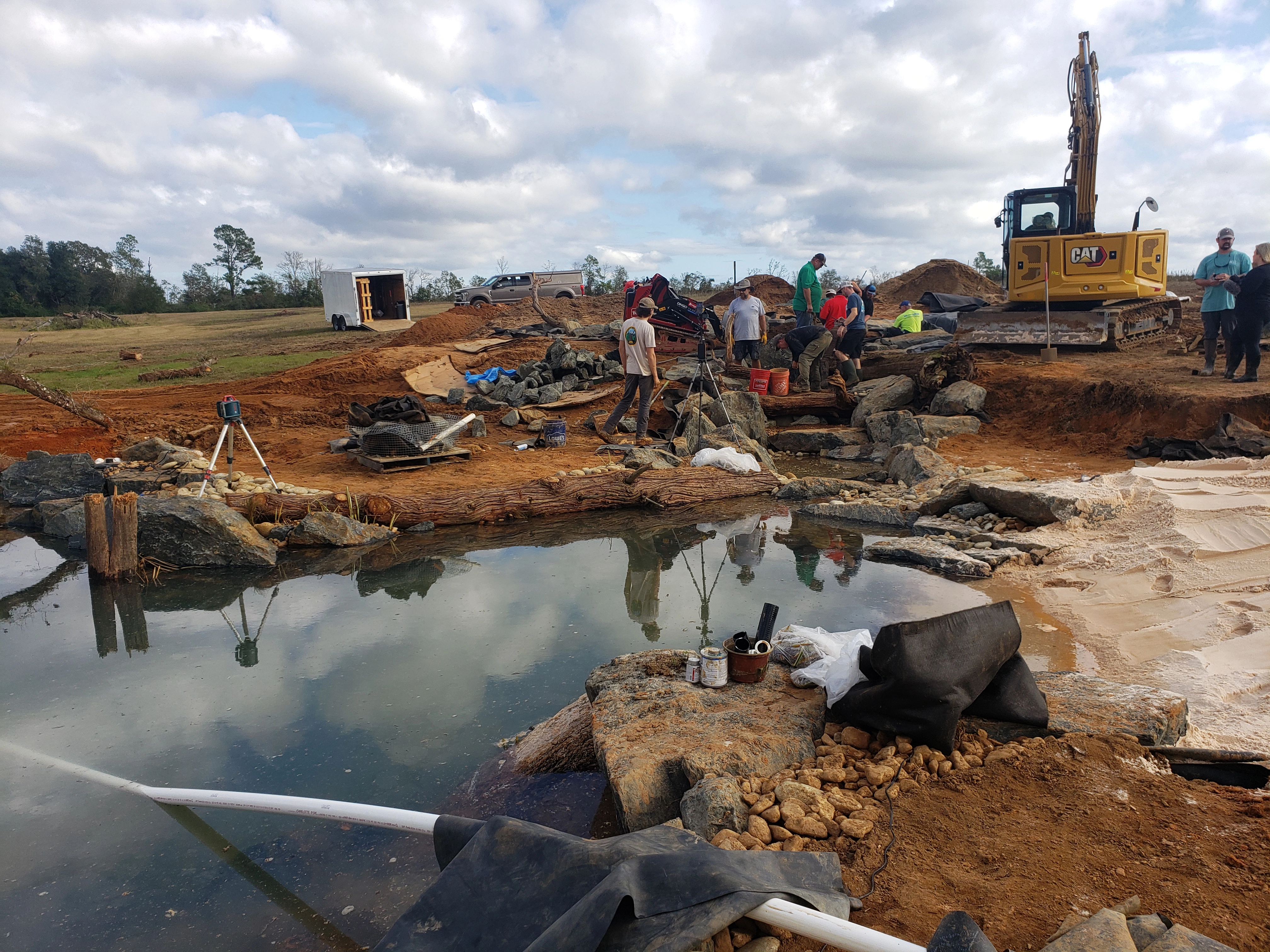 Professional ecosystem pond and waterfall build site with equipment, stone, liner, and crew