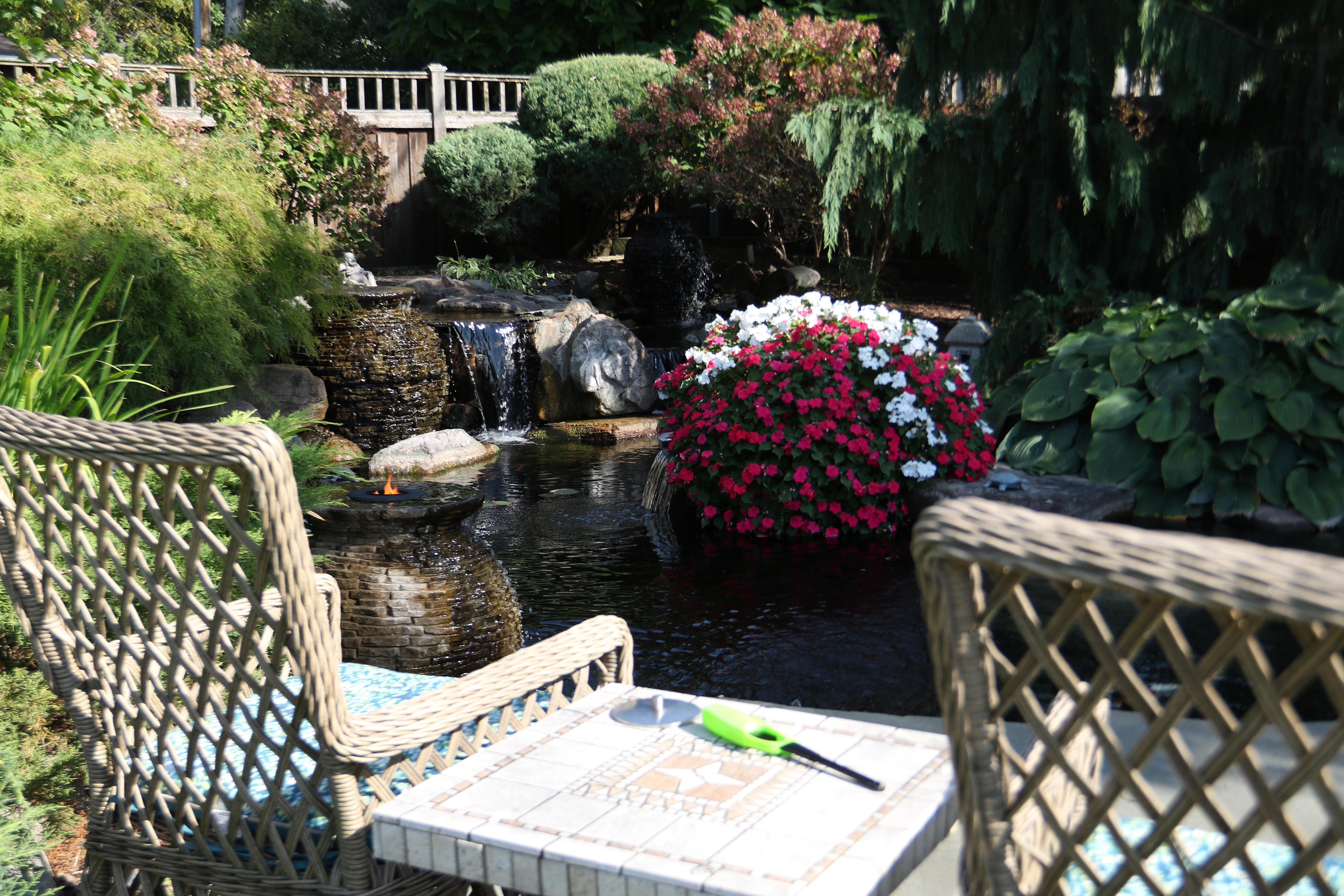 Backyard pond with seating area, waterfall, flowers, and mature landscape