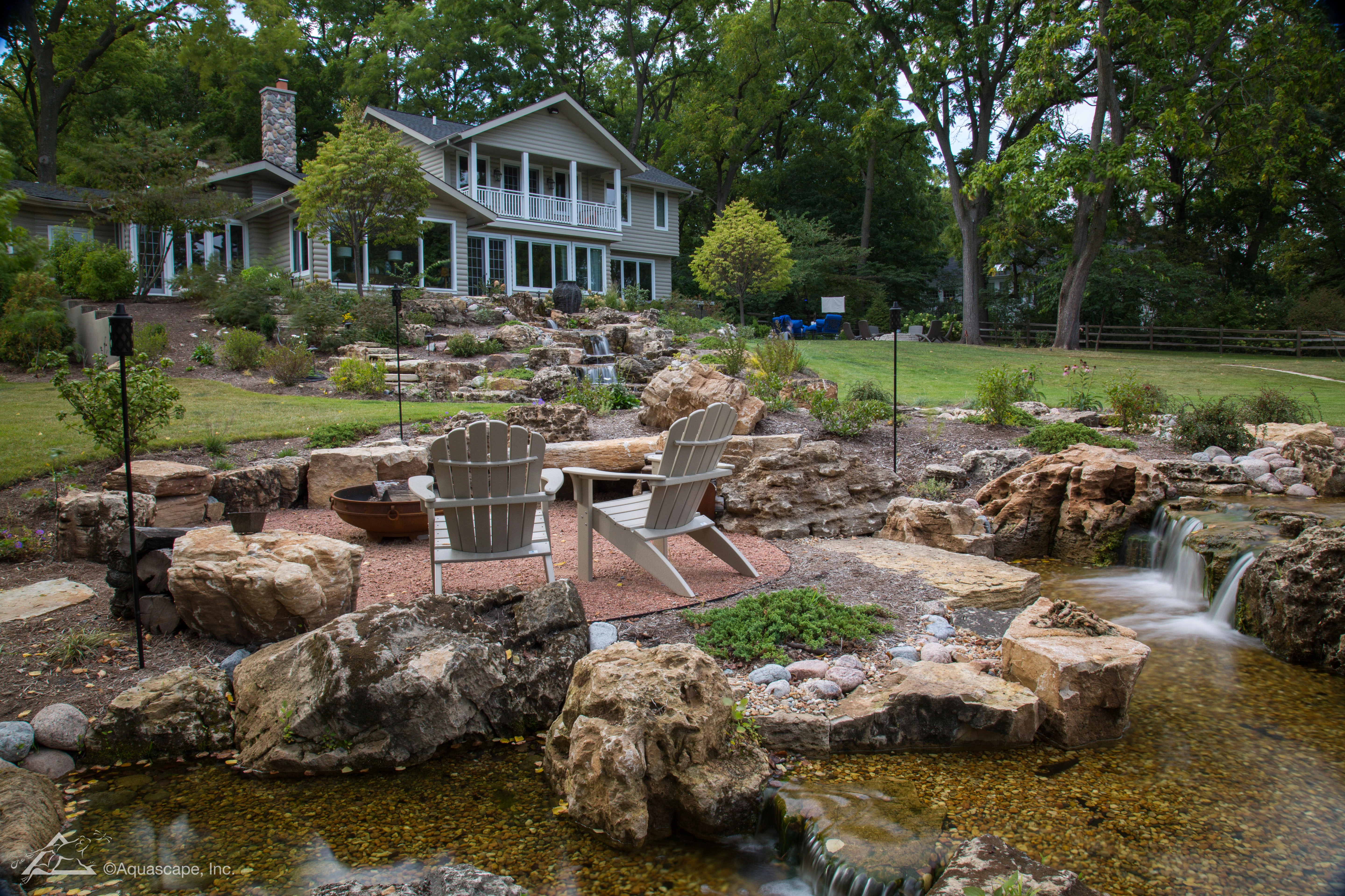 Large custom pondless waterfall with natural stone, seating area, and landscape integration