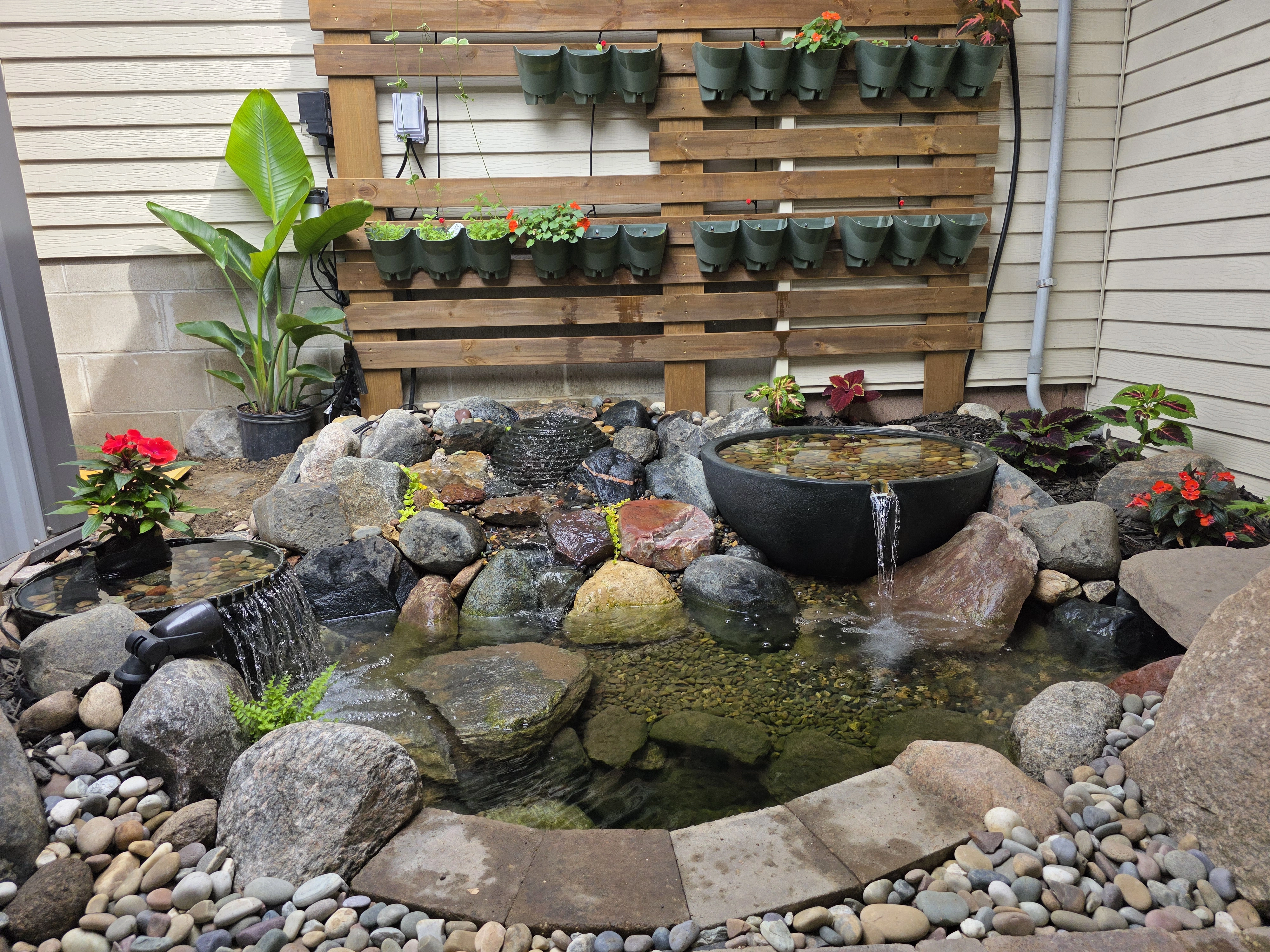 Completed backyard ecosystem pond with waterfall, patio, trellis, and garden in New Ulm, Minnesota